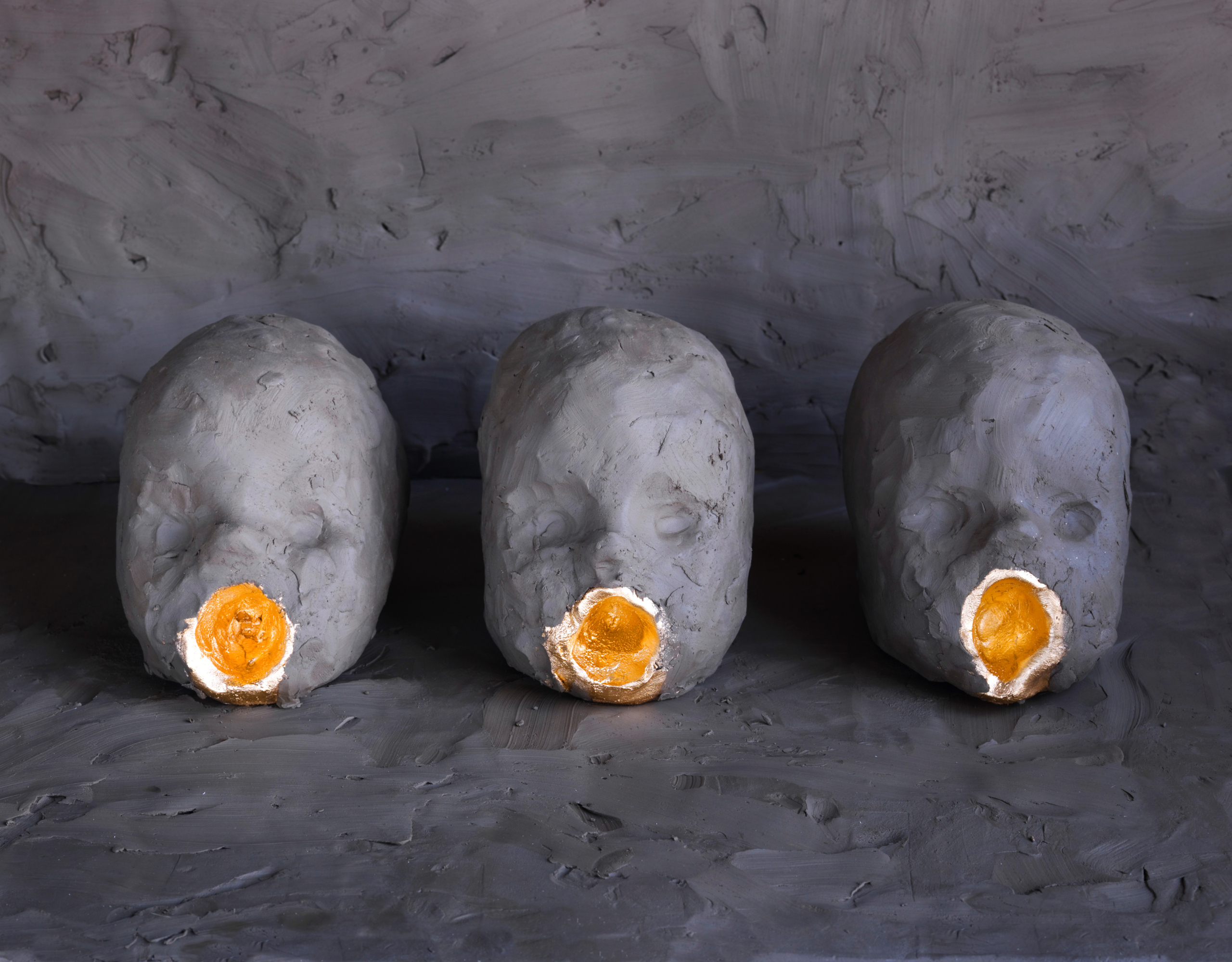 Skulptur föreställande tre barnhuvuden med öppna munnar.